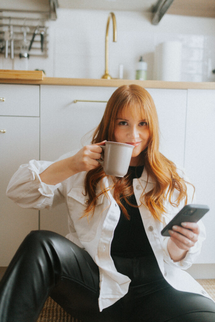 East & Eve Creative Co founder, Madeline Taylor, drinking a coffee and checking her smartphone, while smiling. 