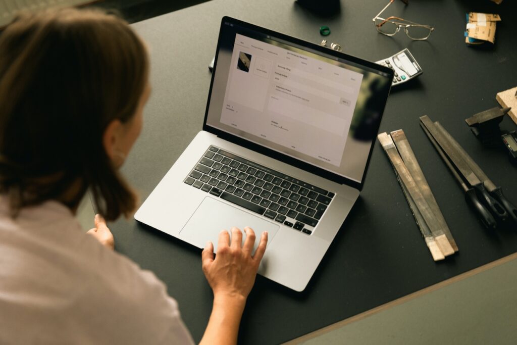 A woman sits at a desk and works on her shop on her laptop. When choosing a website platform, Squarespace was the best fit. She is setting up a listing. 