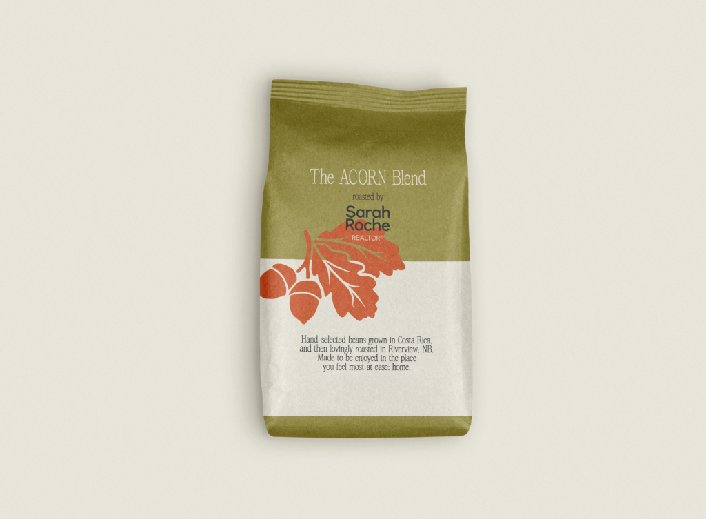 A photo of a custom coffee bean package design with Sarah Roche's branding. The package is soft-touch paper, with green and creamy background, featuring her brand illustrations (two acorns with their leaves attached) - and her primary logo. 